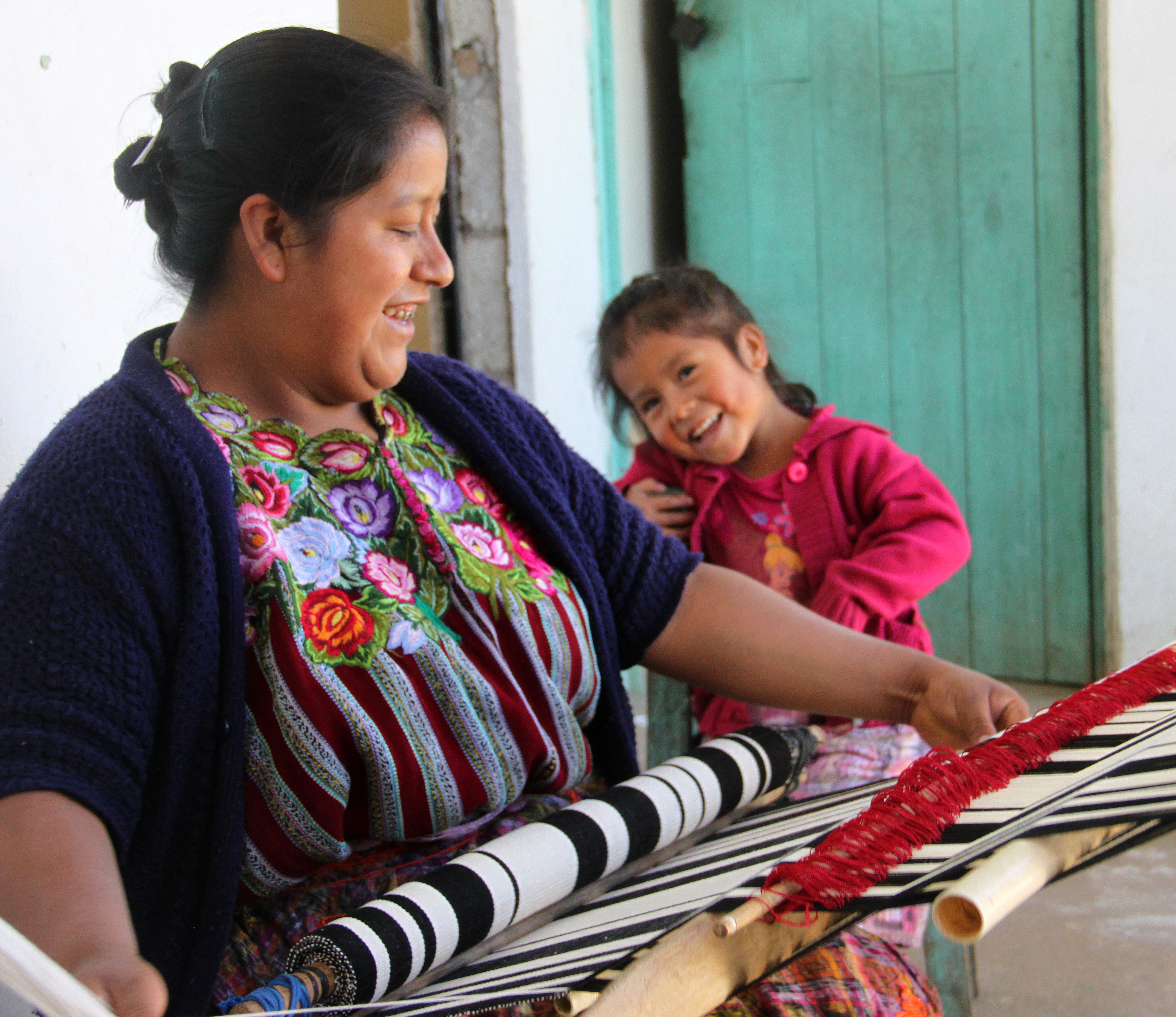 Woman working on loom and smiling at child